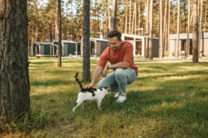 Man crouching on lawn touching cat