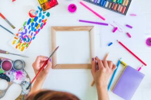 Female Hands holding painting brush over blank canvas with painting materials on white